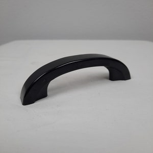 May include: A black plastic handle with a rounded shape.