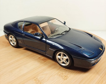 Puede incluir: Un coche modelo de fundición a escala 1/18 de un Ferrari 550 Maranello de color azul oscuro. El coche tiene un interior beige y ruedas plateadas.