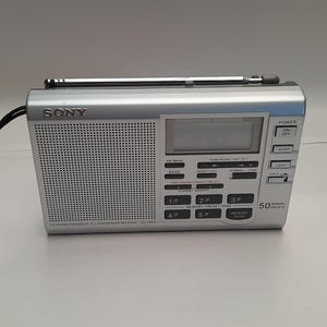 May include: A silver Sony ICF-SW38 radio with a telescopic antenna, a digital display, and a variety of buttons for tuning, time setting, and memory presets. The radio has a black speaker grille and a silver front panel with the Sony logo.