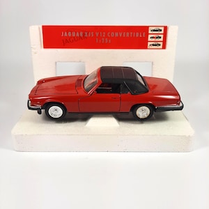 May include: Red Jaguar XJS V12 Convertible diecast model car in 1:25 scale. The car has a black convertible top and is sitting on a white foam base.