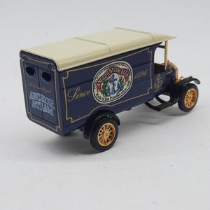 May include: A die-cast model delivery truck in dark blue with a cream-colored roof. The side features the text Anchor Steam Beer, Made in San Francisco since 1896, and an anchor logo. The back displays the text Anchor Steam. It has gold-toned wheels.