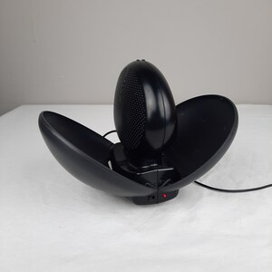 以下が含まれることがあります： コード付きの黒いドーム型のポータブルスピーカー。スピーカーが開いており、上部のドームが持ち上げられています。