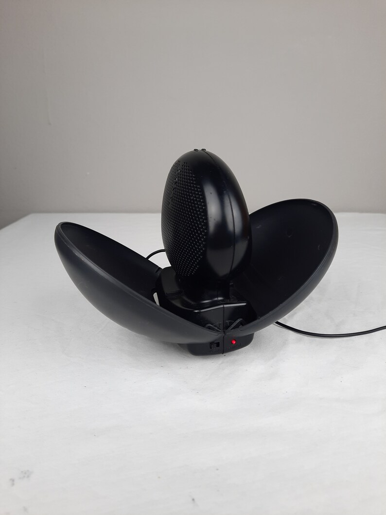 以下が含まれることがあります： コード付きの黒いドーム型のポータブルスピーカー。スピーカーが開いており、上部のドームが持ち上げられています。