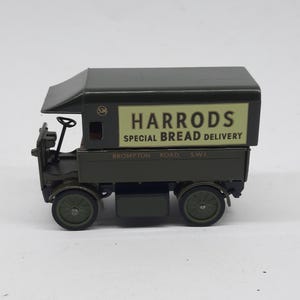 Puede incluir: Un cami&oacute;n de reparto de juguete de metal en color verde oscuro con un panel lateral crema que muestra el texto HARRODS SPECIAL BREAD DELIVERY y BROMPTON ROAD S.W.1. El veh&iacute;culo tiene una cabina abierta, un volante y cuatro ruedas.