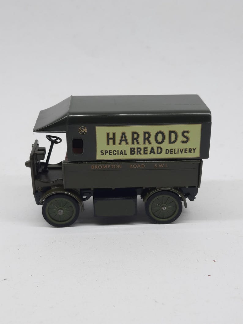 Puede incluir: Un cami&oacute;n de reparto de juguete de metal en color verde oscuro con un panel lateral crema que muestra el texto HARRODS SPECIAL BREAD DELIVERY y BROMPTON ROAD S.W.1. El veh&iacute;culo tiene una cabina abierta, un volante y cuatro ruedas.