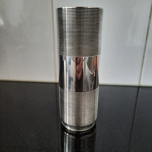 May include: A silver cylindrical vase with a textured, ribbed design. The vase is polished and reflective.