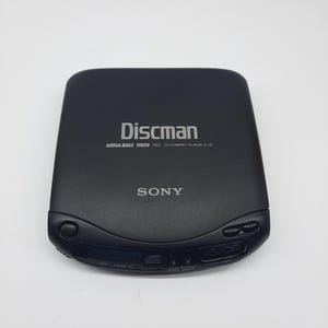 Puede incluir: Reproductor de CD compacto Sony Discman negro. El dispositivo tiene la palabra "Discman" impresa en la parte superior, junto con "MEGA BASS" y "CD COMPACT PLAYER D-131". La palabra "SONY" está impresa debajo de "Discman".