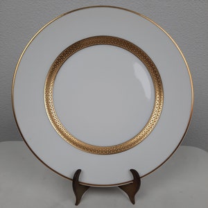 Puede incluir: Plato de cena de cer&aacute;mica blanca con un borde dorado y una banda decorativa dorada alrededor del centro.