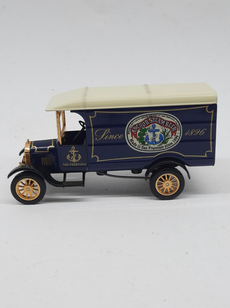 May include: A blue and cream-colored vintage delivery truck model featuring gold-toned wheels and an anchor logo. The side panel displays the text "Since 1896" and a circular emblem reading "Anchor Steam Beer, Made in San Francisco since 1896".