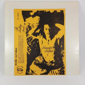 May include: A vintage vinyl record album cover featuring a yellow and black design. The cover has the text "Beautiful Delilah" and "The Rolling Stones." The album cover is in a white sleeve.