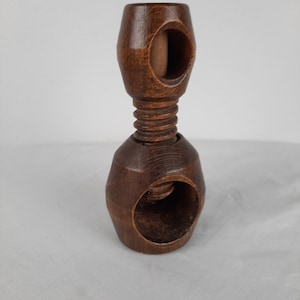 May include: A dark brown wooden nutcracker with a screw mechanism. The nutcracker is made of two pieces of wood that are joined together by a screw. The top piece of wood has a hole in the center, and the bottom piece of wood has a hole on the side. The screw is used to crush the nuts.