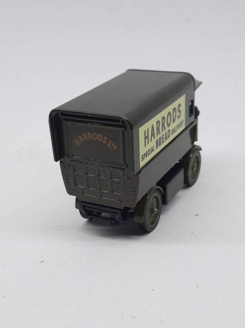 Puede incluir: Un cami&oacute;n de reparto de juguete de metal fundido en color verde oscuro con un panel lateral crema que muestra el texto HARRODS SPECIAL BREAD DELIVERY y el texto HARRODS LTD en la puerta trasera. El veh&iacute;culo tiene cuatro ruedas verdes.