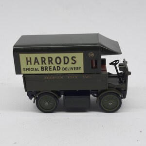 Puede incluir: Un cami&oacute;n de reparto de juguete de estilo antiguo en color verde oscuro con un panel lateral crema que muestra el texto HARRODS SPECIAL BREAD DELIVERY y BROMPTON ROAD S.W.1. El veh&iacute;culo tiene una cabina abierta, un volante y cuatro ruedas.