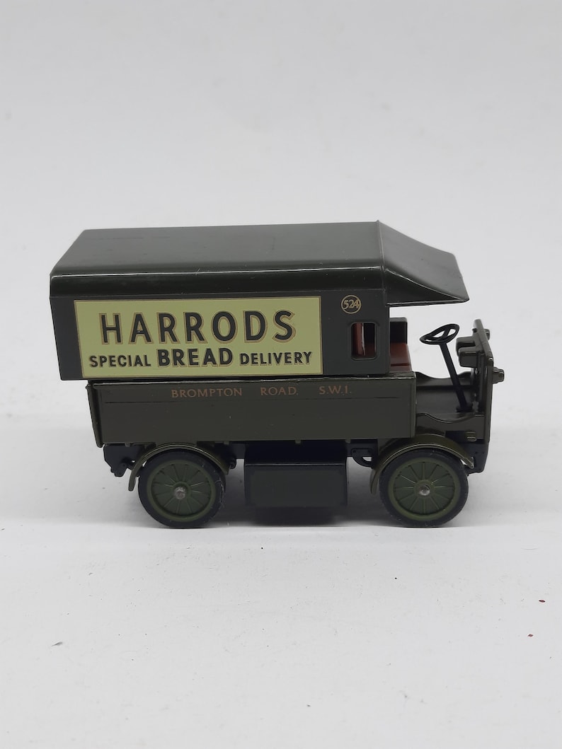 Puede incluir: Un cami&oacute;n de reparto de juguete de estilo antiguo en color verde oscuro con un panel lateral crema que muestra el texto HARRODS SPECIAL BREAD DELIVERY y BROMPTON ROAD S.W.1. El veh&iacute;culo tiene una cabina abierta, un volante y cuatro ruedas.