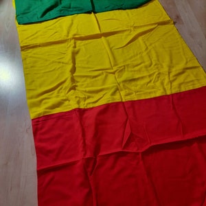May include: A rectangular flag with three horizontal stripes: green at the top, yellow in the middle, and red at the bottom. The flag is made of fabric and lies flat, with visible folds.