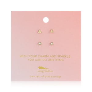 May include: A pink card displays two sets of gold-colored post earrings. One set features three small beads, and the other has a square, clear stone. The card has gold text that reads "WITH YOUR CHARM AND SPARKLE, YOU CAN DO ANYTHING" and "Lucky Feather."