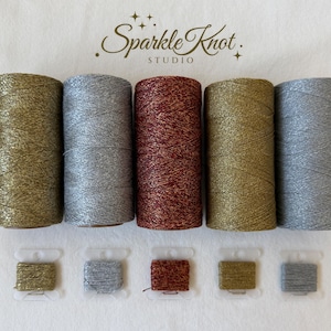 May include: Five large spools of metallic thread in gold, silver, copper, bronze, and light silver, accompanied by five matching small plastic bobbins. The text Sparkle Knot STUDIO is centered above the spools on a plain off-white background.
