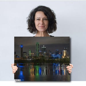 May include: A nighttime cityscape of Dallas, Texas, with the iconic Reunion Tower and other skyscrapers illuminated in blue and green lights. The city skyline is reflected in the water below.