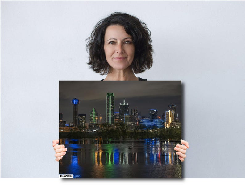May include: A nighttime cityscape of Dallas, Texas, with the iconic Reunion Tower and other skyscrapers illuminated in blue and green lights. The city skyline is reflected in the water below.