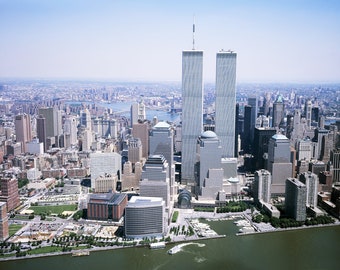 May include: An aerial view of the Twin Towers of the World Trade Center in New York City. The towers are tall and slender, with a blue sky in the background. The city skyline is visible in the distance.