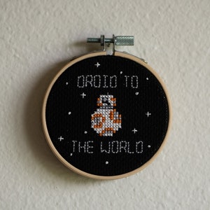 May include: A black and white embroidered hoop with a white droid character and the text "Droid to the world".
