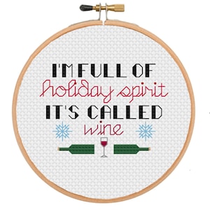 May include: A white embroidery hoop with the text "I'm full of holiday spirit it's called wine" in black and red lettering. Two snowflakes are on either side of the word "wine". A wine glass and two wine bottles are below the text.