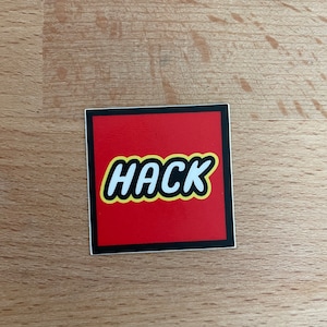 May include: A red Lego brick with a black border and the word "HACK" printed in white with a yellow outline.
