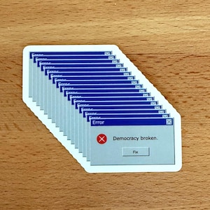 May include: A stack of blue and white stickers with a Windows error message that reads "Democracy broken." The message has a red X and a button that says "Fix."