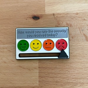 以下が含まれることがあります： 「今日のセキュリティの評価はどうですか？」というテキストと、緑、黄、オレンジ、赤の4つのスマイリーフェイスが描かれた白いフィードバックカード。黒い三角形のポインターがオレンジのスマイリーフェイスを指しています。