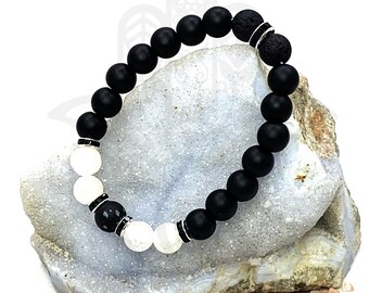May include: Black and white beaded bracelet with a lava bead and silver accents. The bracelet is on a blue and white rock with pink salt crystals.