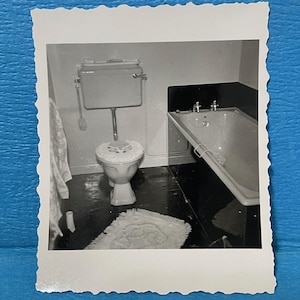 May include: A black and white photo of a bathroom with a white toilet and a white bathtub. The toilet has a white seat and a white tank. The bathtub has a white tub and a white faucet.