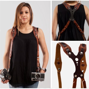 May include: A brown leather camera strap with adjustable straps and a Y-shaped back support. The strap is designed to distribute weight evenly across the shoulders.