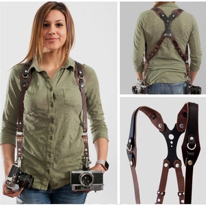 May include: A brown leather camera strap with a black adjustable chest strap. The strap has metal buckles and rings. The strap is shown being worn by a person and also laid flat.