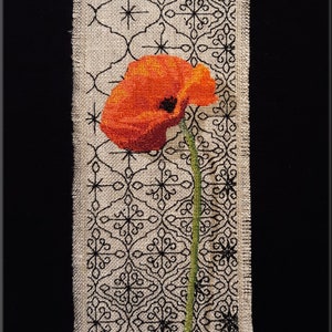 May include: A red poppy flower with a green stem is embroidered on a beige fabric with a black geometric pattern.