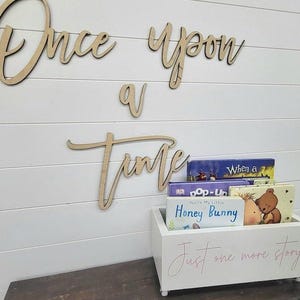 May include: Wooden sign with the words "Once upon a time" above a white box filled with children's books. The box has the text "Just one more story" in pink script.