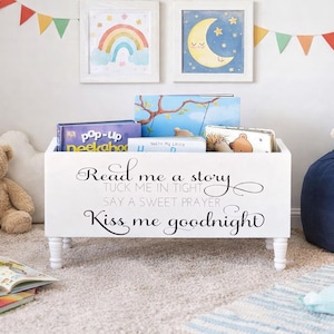 May include: A white wooden bookshelf with books, a teddy bear, and a lamb plushie. The bookshelf has the text "Read me a story, Tuck me in tight, Say a sweet prayer, Kiss me goodnight." Two framed pictures and a colorful banner are on the wall.