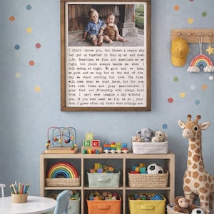 May include: A child's playroom with a light blue wall, featuring a framed photo with text, a wooden shelf filled with toys, and a giraffe. The shelf holds baskets, blocks, and a rainbow. A small table and chair are in the foreground.