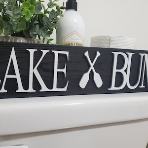 May include: A handmade wooden sign with the text "Welcome" in a handwritten style. The sign is painted white with a distressed finish, and a small green leaf is attached to the top. The sign is designed for home decor.