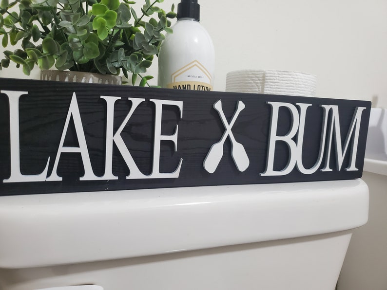 May include: A handmade wooden sign with the text "Welcome" in a handwritten style. The sign is painted white with a distressed finish, and a small green leaf is attached to the top. The sign is designed for home decor.
