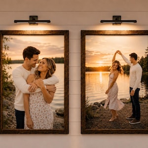 May include: Two framed landscape photos with a warm, rustic wooden frame. Each photo depicts a couple in a romantic setting near a lake at sunset. The frames are mounted on a white wall with a black light fixture above each.