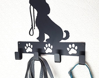 May include: Black metal dog leash holder featuring a dog silhouette holding a leash. The holder has three hooks below paw print cutouts, with a leash and a collar hanging from the hooks. A decorative item for pet owners.