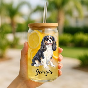 May include: A clear glass tumbler with a wooden lid and a glass straw. The tumbler is filled with a yellow liquid and lemon slices. A Cavalier King Charles Spaniel illustration is on the front, with the name "Georgia" in script.