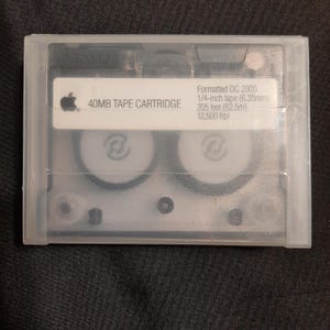 May include: A clear plastic case containing a 40MB tape cartridge for a computer. The label on the cartridge reads "Formatted DC 2000 1/4-inch tape (6.35mm) 205 feet (62.5m) 12,500 ftpi".