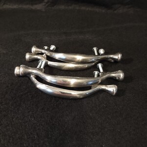 May include: Four silver cabinet door pulls with a curved design. The pulls are stacked on top of each other.