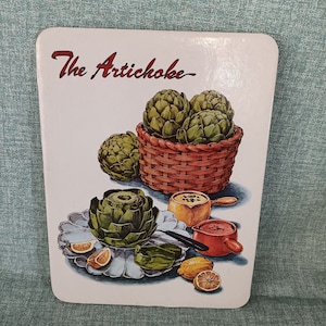May include: A white ceramic trivet with a green and brown illustration of artichokes, lemons, and a bowl of artichoke hearts. The text "The Artichoke" is written in red at the top of the trivet.