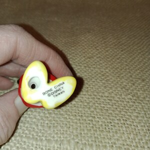May include: A yellow and red ceramic figurine with the text "Bone China &copy;Disney Taiwan" on the bottom.