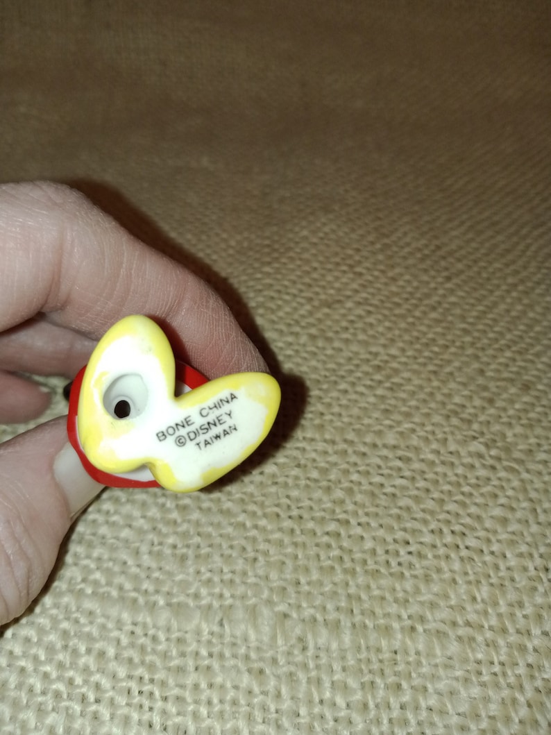 May include: A yellow and red ceramic figurine with the text "Bone China &copy;Disney Taiwan" on the bottom.
