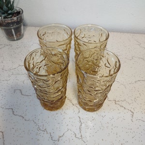 May include: Set of four amber glass tumblers with a textured, rippled design. The glasses are empty and sitting on a white countertop.