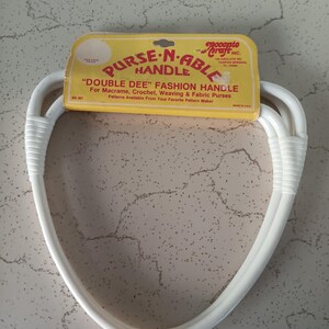 May include: A white "Double Dee" fashion purse handle with a yellow and red label. The label reads "PURSE-N-ABLE HANDLE" and "DOUBLE DEE" FASHION HANDLE. The handle is designed for macrame, crochet, weaving, and fabric purses.