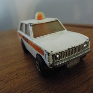 May include: White toy police car with an orange light on top. The car has a silver grill and a black bumper. The word "Police" is printed on the side of the car.